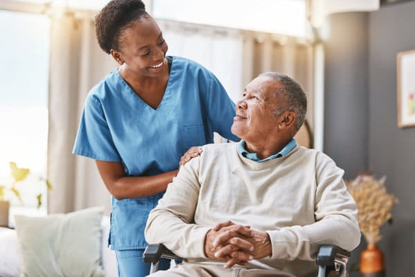 Elderly man sitting in a wheelchair, accompanied by health personnel