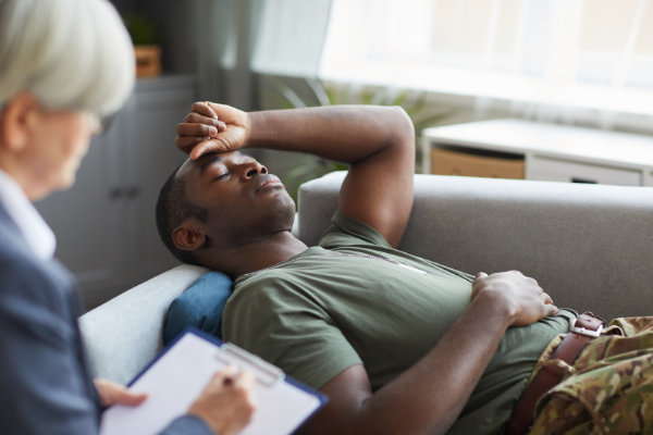 War veteran sitting on a therapist's couch, placing his hand on his head in distress